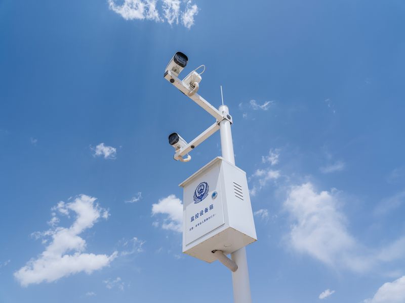 Deux caméras de sécurité blanches montées sur un mât sous ciel bleu nuageux