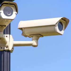 Caméra de surveillance extérieure blanche montée sur mât noir sous ciel bleu